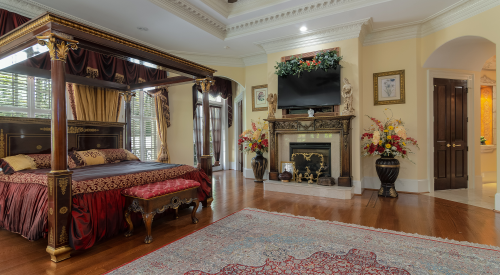 Luxurious bedroom with a four-poster bed, elegant decor, a fireplace, and floral arrangements. Rich wood flooring.