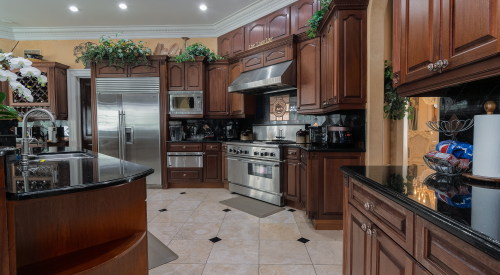 A spacious kitchen with dark wood cabinets, stainless steel appliances, and a black granite countertop.