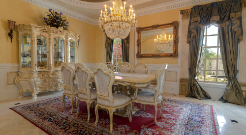 Elegant dining room featuring a large ornate table, plush chairs, a crystal chandelier, and decorative furnishings.