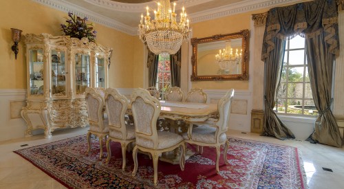 Elegant dining room featuring a large ornate table, plush chairs, a crystal chandelier, and decorative furnishings.