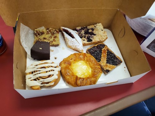 A box of assorted pastries, including a cinnamon roll, fruit bars, and a cheese danish, on a red table.