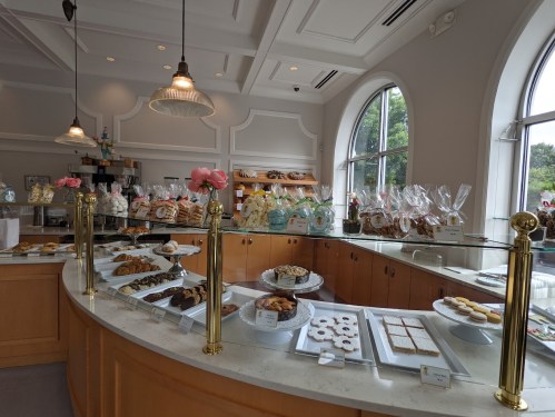 A bright bakery display featuring various cookies and pastries in glass cases, with decorative flowers and a cozy atmosphere.