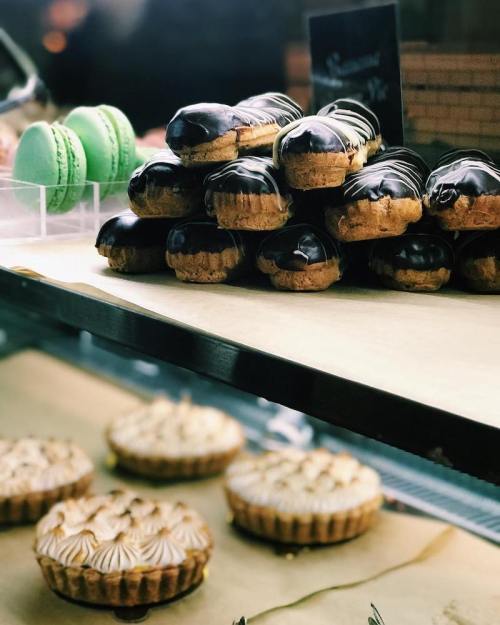 A display of desserts featuring chocolate-covered pastries, green macarons, and meringue-topped tarts.