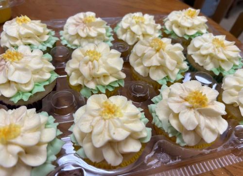 A tray of beautifully decorated cupcakes topped with flower-shaped frosting in cream and green colors.