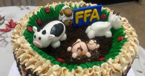 A decorated cake featuring farm animal figurines, green frosting, and an "FFA" sign on top.