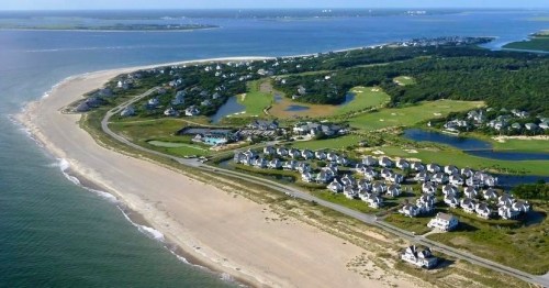 Aerial view of a coastal area with sandy beaches, green landscapes, and residential homes along the shoreline.