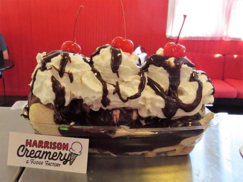 A large ice cream sundae with three scoops, whipped cream, chocolate sauce, and cherries on top, served in a dish.
