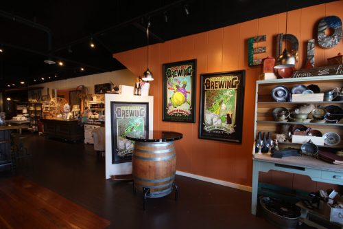 Interior of a shop featuring brewing posters, wooden shelves with various items, and a barrel table.