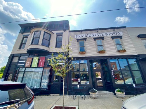 Exterior of Prairie State Winery, featuring large windows, outdoor seating, and a bright sky above.