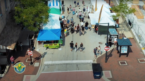 Aerial view of a bustling street market with colorful tents and crowds of people enjoying the event.