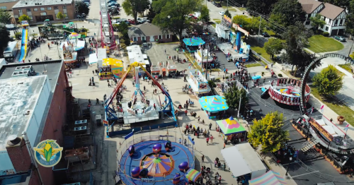 Aerial view of a vibrant fairground with rides, games, and crowds enjoying a sunny day.