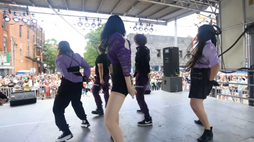 A dance group performs on stage in front of a large crowd at an outdoor event.