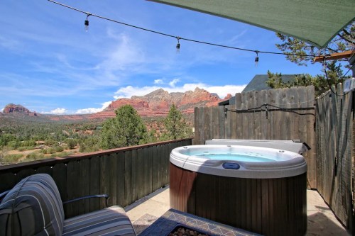 A hot tub on a patio with a scenic view of red rock formations and trees under a blue sky.