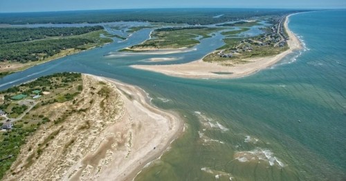 Aerial view of a coastal landscape with sandy beaches, winding waterways, and lush greenery in the background.