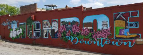 Colorful mural reading "Welcome to Monroe Downtown," featuring flowers and local imagery on a brick wall.