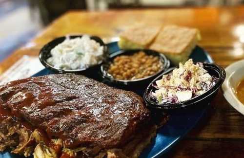 A plate of barbecue ribs with sides of coleslaw, baked beans, potato salad, and cornbread.