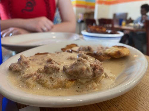 A plate of biscuits topped with creamy sausage gravy, with a blurred background of a restaurant setting.