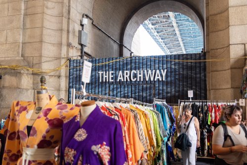 A vibrant market scene with colorful clothing racks and a sign reading "THE ARCHWAY" in the background.