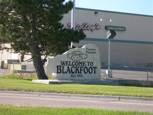 Welcome sign for Blackfoot, established 1901, with a large rock and "Famous Potatoes" inscription in front of a store.