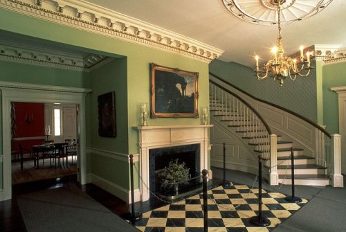 Elegant foyer with a checkered floor, chandelier, and a staircase, featuring green walls and classic decor.