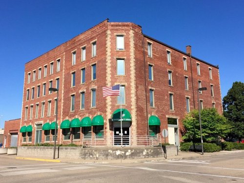A brick building with green awnings and an American flag, set against a clear blue sky.