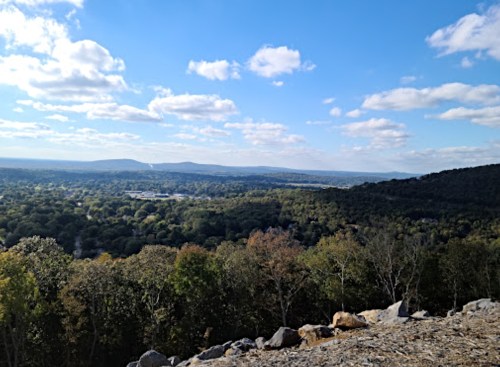 A panoramic view of rolling hills and valleys under a blue sky with scattered clouds.