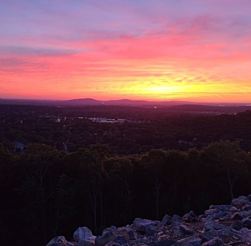 A vibrant sunset over rolling hills, casting warm colors across the sky and illuminating the landscape below.