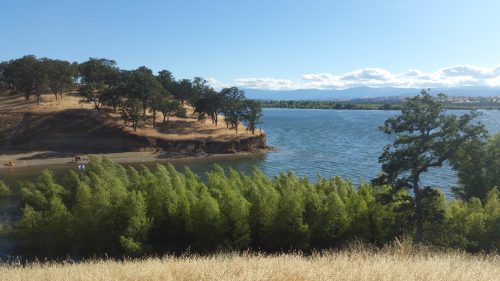 A serene lake surrounded by green trees and rolling hills under a clear blue sky.