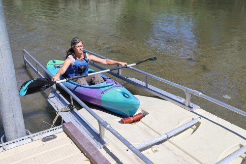 A person in a kayak approaches a dock on a calm river, preparing to exit the water.