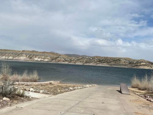 A serene lake view with a concrete ramp leading to the water, surrounded by hills and cloudy skies.