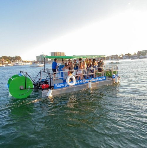 A party boat with people enjoying a sunny day on the water, featuring a green paddle wheel and a scenic backdrop.