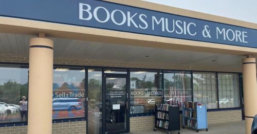 Exterior of a store labeled "Books Music & More," featuring a display of books and records in the window.