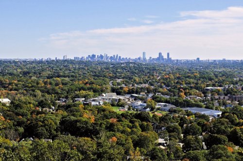 A panoramic view of a city skyline surrounded by lush green trees and colorful autumn foliage.