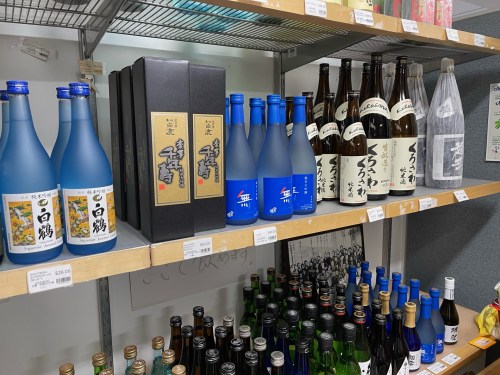 A shelf displaying various bottles of sake, including blue and clear bottles, with a black box set in the center.