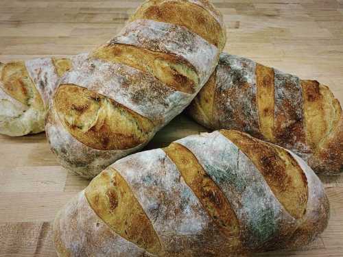 Four freshly baked loaves of bread with a golden crust and scored tops, resting on a wooden surface.