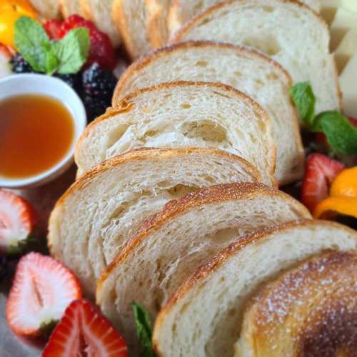 Sliced bread arranged on a platter with fresh berries, mint, and a small bowl of syrup.