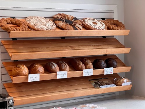A wooden display shelf with various types of bread, including loaves and pastries, labeled with prices.