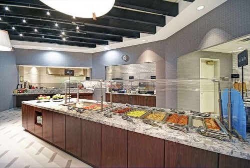A modern buffet with a variety of colorful dishes displayed on a marble countertop in a well-lit dining area.