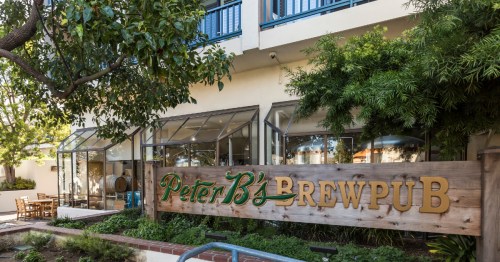 Exterior view of Peter B's Brewpub, featuring a wooden sign and outdoor seating surrounded by greenery.