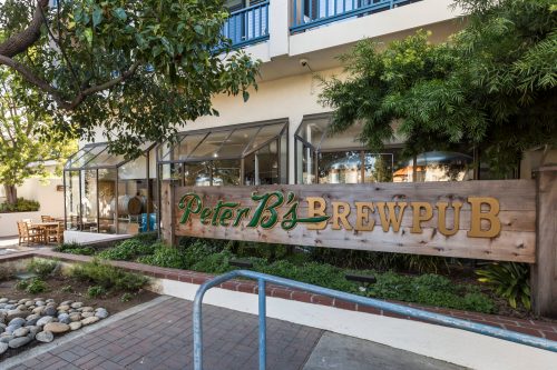 Sign for Peter B's Brewpub outside a building, surrounded by greenery and outdoor seating.