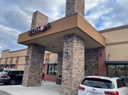 Exterior view of a building with a sign reading "BLOSSOM," featuring stone pillars and a parking area.