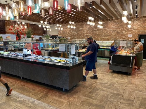 A spacious buffet restaurant with various food stations and customers serving themselves. Bright lights and wooden decor.