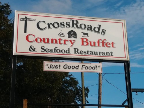 Sign for CrossRoads Country Buffet & Seafood Restaurant, featuring the slogan "Just Good Food!" against a blue sky.