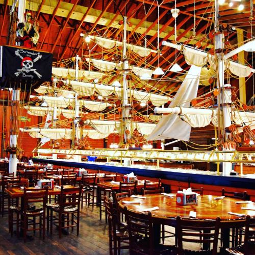 Interior of a themed restaurant featuring a large ship replica, wooden tables, and pirate decor.
