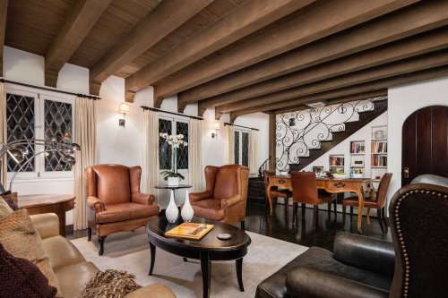 Cozy living room with leather chairs, wooden beams, and a staircase, featuring a dining area and decorative accents.