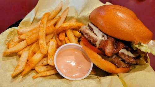 A juicy burger with bacon, lettuce, and sauce, served with a side of seasoned fries and dipping sauce.