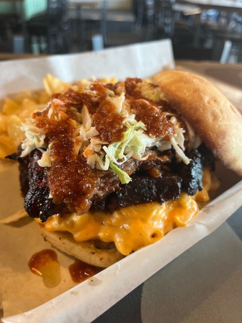 A close-up of a burger topped with pulled pork, coleslaw, and sauce, served with a side of fries.