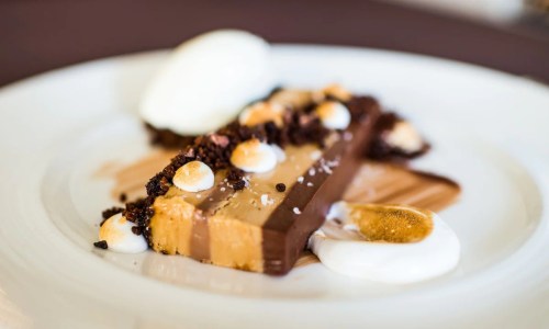 A slice of layered dessert with chocolate, caramel, and meringue, garnished with cream and a scoop of ice cream.