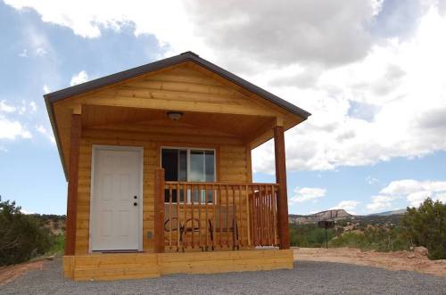 A small wooden cabin with a porch, set against a blue sky and distant hills.