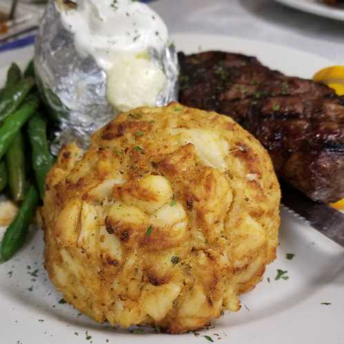 A plate featuring a baked potato with sour cream, green beans, a grilled steak, and a large crab cake.